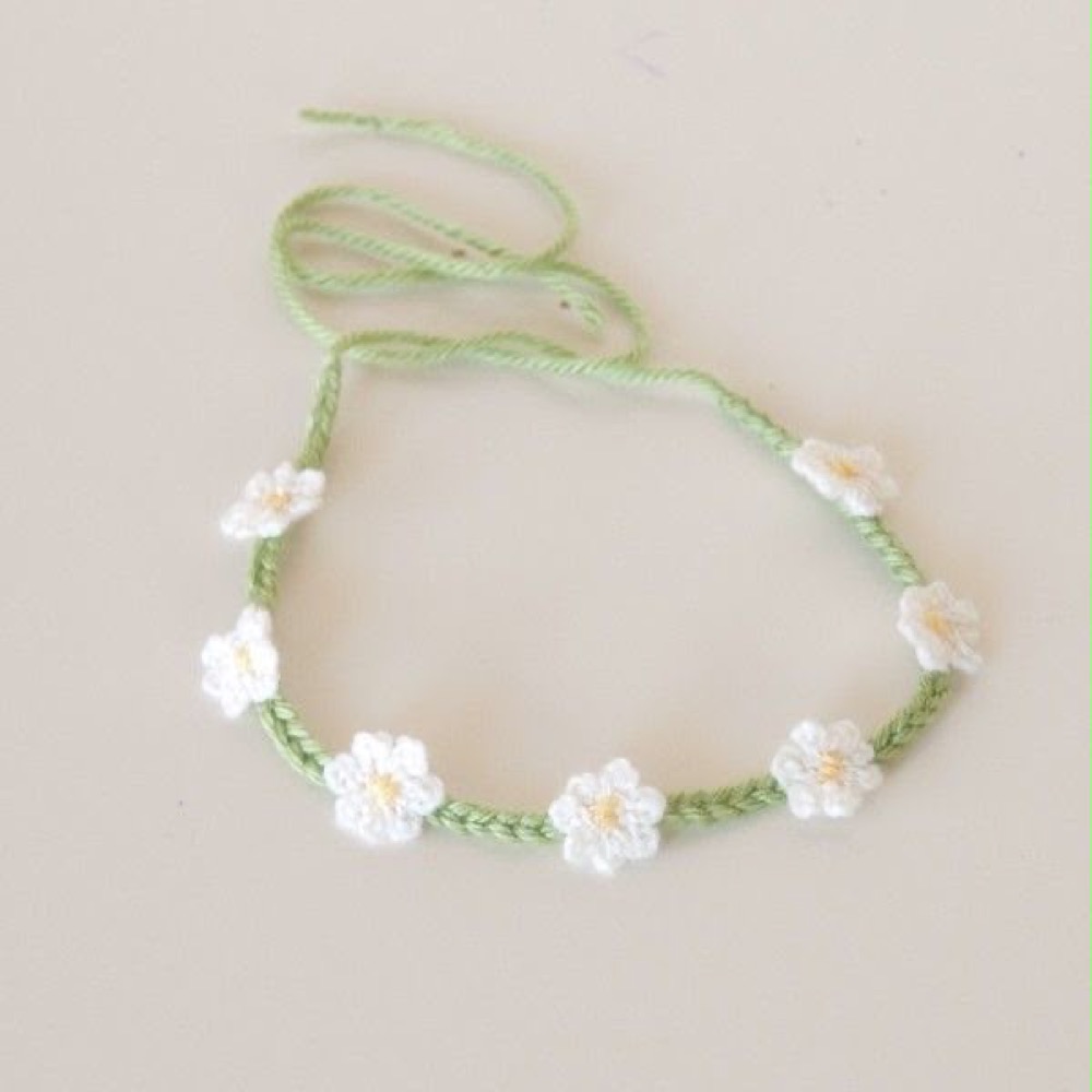 Handmade crochet daisy chain rakhi with white flowers on a green thread