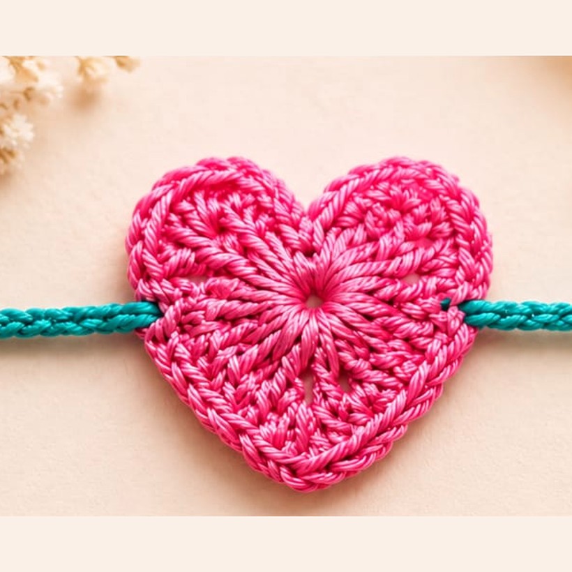 Handmade crochet pink heart rakhi on a teal thread
