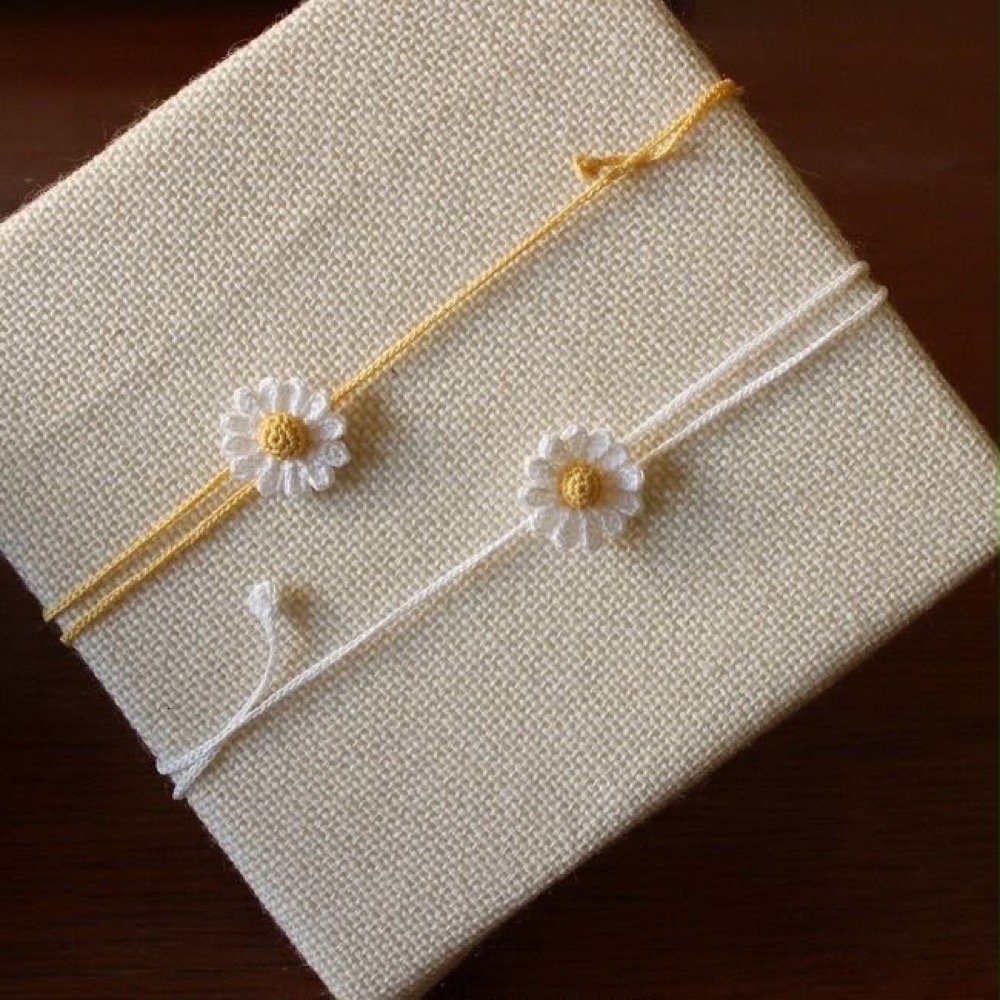 Two delicate handmade mini daisy rakhis on slim yellow and white threads