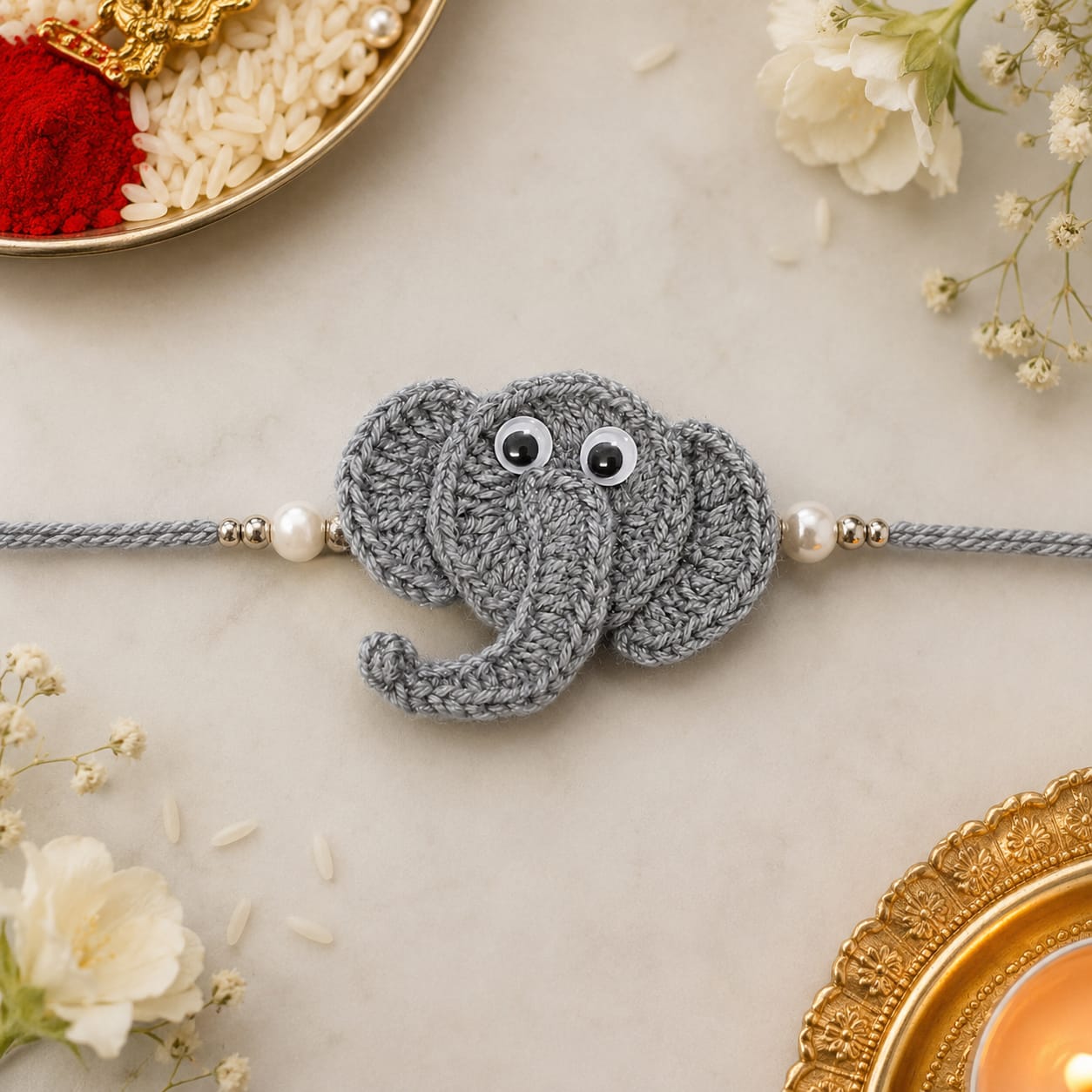 Handmade crochet grey elephant face rakhi with white tusks on a beaded grey cord