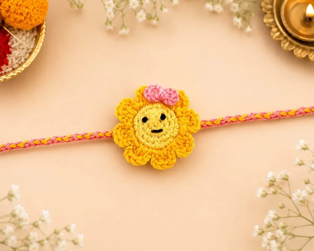 Handmade crochet smiley sunflower face rakhi with a pink bow on a pink-and-yellow braided thread